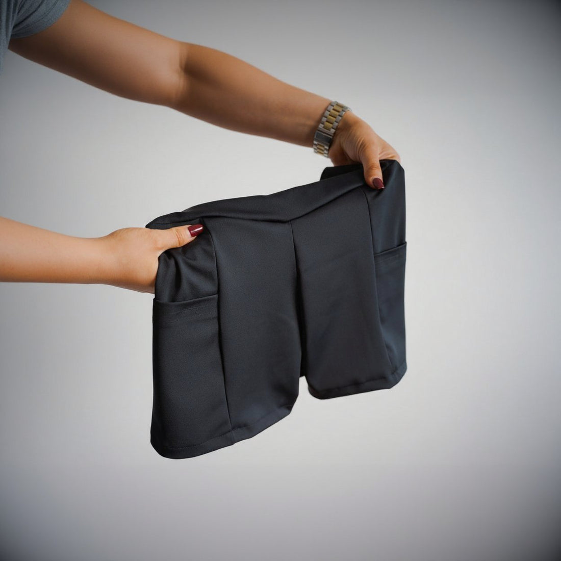Black shorts held by a person against a neutral background
