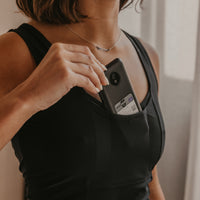 Woman holding an Omnipod controller in her black Mude Tank top with a blurred background