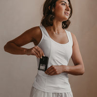 Woman wearing a white Mude Tank top and light grey pants against a beige background