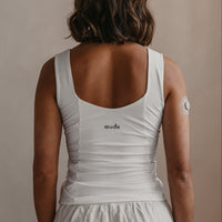 Person wearing a white Mude tank top with 'mude' branding on a beige background
