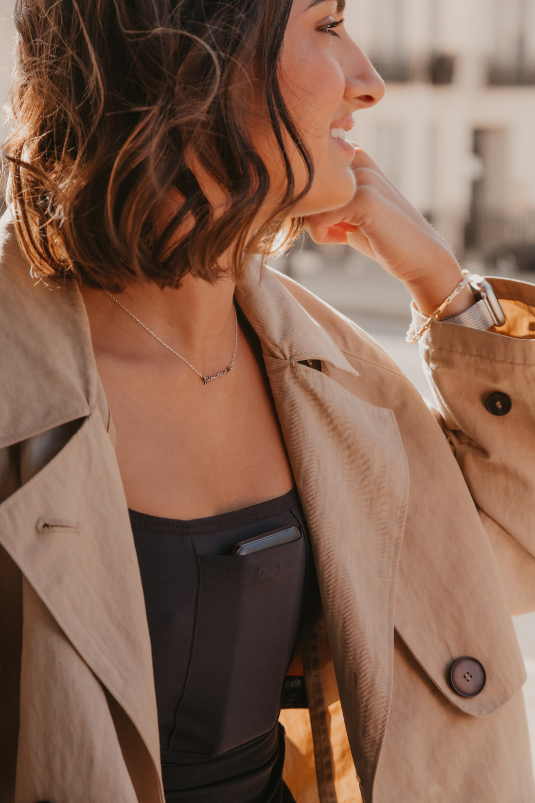 Woman wearing a beige trench coat over a black Mude Tank top with a blurred background