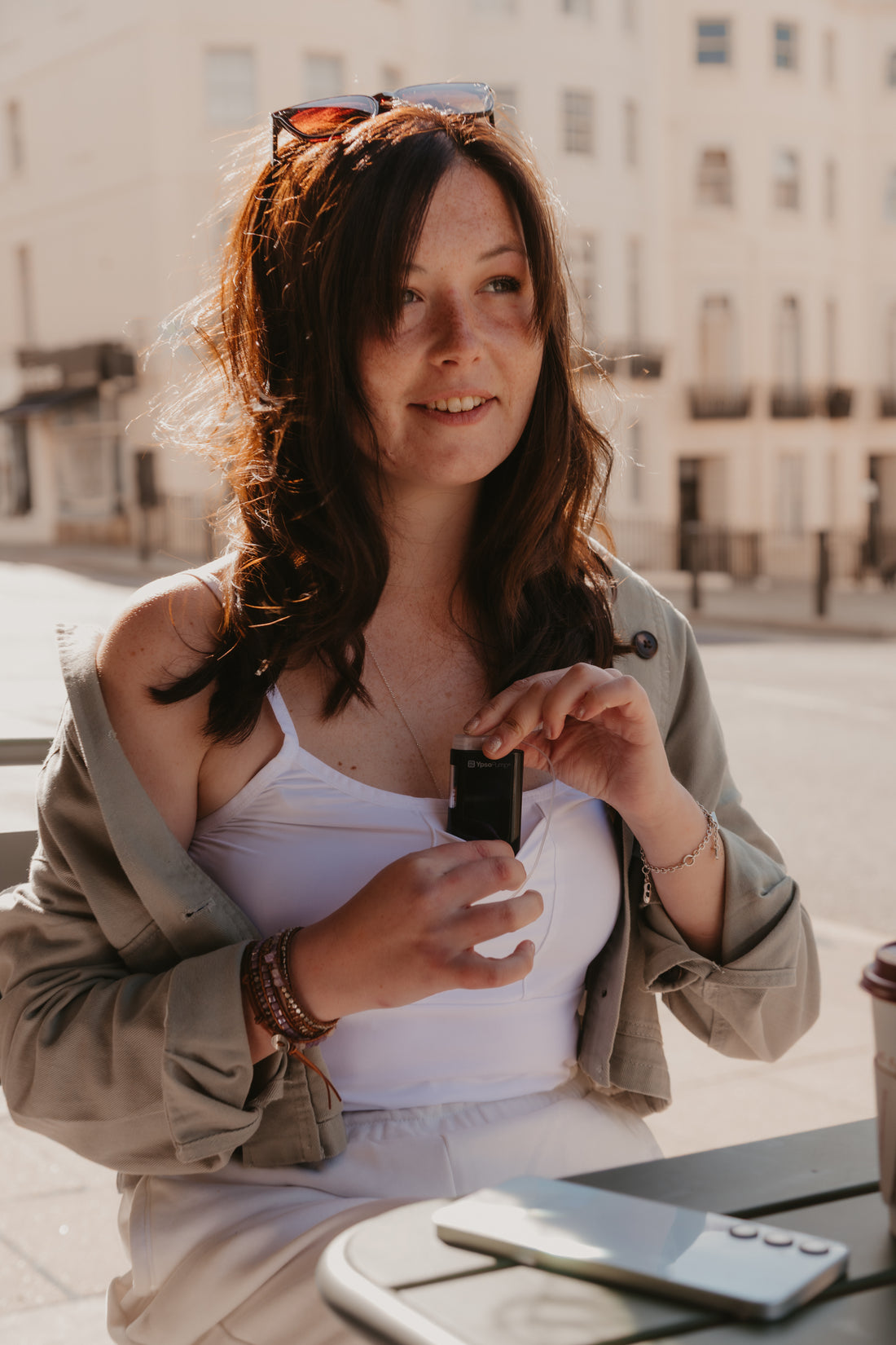 Woman placing an insulin pump into her white Mude Camisole top outdoors with a blurred background.
