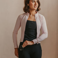 Woman wearing a light pink cardigan over a black Mude Tank and black Mude Shorts, standing against a beige wall with white vases.